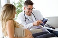 Young male gynecologist doctor showing to pregnant woman ultrasound scan baby with digital tablet.