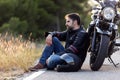 Young male sitting on the road, leaning on his motorcycle while waiting to the roadside assistance to repair the motorbike Royalty Free Stock Photo