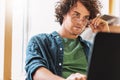 Shot of a young man with curly hair sitting at table looking at laptop and thinking. Royalty Free Stock Photo