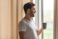 Shot of a young man having a cup of coffee while looking out of the window at home. Royalty Free Stock Photo