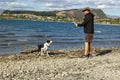 Shot of young man playing with his dog on the bank of lake Wanaka with iconic lone tree. South island of New Zealand. Royalty Free Stock Photo