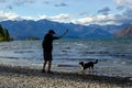 Shot of young man playing with his dog on the bank of lake Wanaka with iconic lone tree. South island of New Zealand. Royalty Free Stock Photo