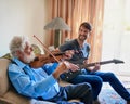 Bonding through their music. Shot of a young man playing the electric guitar while his elderly grandfather plays the Royalty Free Stock Photo