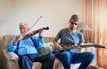 Music bridges the generation gap. Shot of a young man playing the electric guitar while his elderly grandfather plays Royalty Free Stock Photo