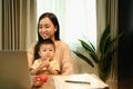 Shot of a young mother having video call with her clients over laptop and carrying her baby on laps Royalty Free Stock Photo