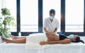 Young physiotherapist woman massaging tummy on pregnant woman on a stretcher at home. Women wearing surgical mask and new normal Royalty Free Stock Photo