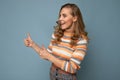 Shot of young positive happy smiling blonde curly woman wearing striped pullover isolated on blue background with copy Royalty Free Stock Photo