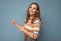 Shot of young positive happy smiling blonde wavy-haired woman wearing striped pullover isolated on blue background with Royalty Free Stock Photo