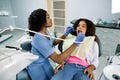 Shot of young pretty female african dentist in blue uniform, making dental check up and caries treatment with drill for