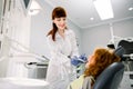 Shot of young pretty female Caucasian dentist in white uniform, making dental check up and caries treatment with drill