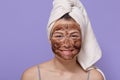 Shot of young smiling woman applying brown cosmetic mask on her face, cleansing her skin at home, uses scrub for facial skin care Royalty Free Stock Photo