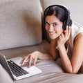 Staying in touch in the digital age. Shot of a young woman on a sofa wearing headphones and using a laptop.