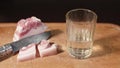 Shotglass and bacon are on wodden cutting board. Man`s hand pours vodka from bottle, takes it and then he eats slice of