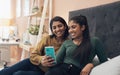 Should I swipe left or right. Shot of two young women looking at something on a cellphone while sitting on a bed Royalty Free Stock Photo