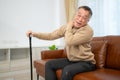 senior guy sits on a sofa with a walking stick in his living room at home Royalty Free Stock Photo