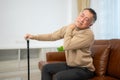 senior guy sits on a sofa with a walking stick in his living room at home Royalty Free Stock Photo