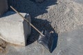 Shovel, leaning against concrete block next to pile of gray gravel, and tracks of truck tires are visible on cement floor screed.