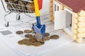 A shovel with a ruble coin rests on a money cart, a number of apartment bills and a toy house Royalty Free Stock Photo