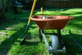 Shovle leaning on a wheelbarrow filled with dirt and a trowle