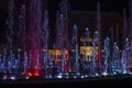 Show of multi-colored musical fountains in siren tones at night Sirik against shops, horizontal