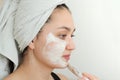 Young woman with a white towel on her head after a shower makes a clay mask on her face Royalty Free Stock Photo