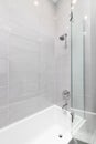 A shower with grey tiles and white bathtub.