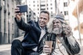 Smiling businessmen in dark costume making selfie with happy homeless