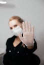 Showing STOP sign with hand by blurred woman in white medical mask and transparent gloves. Selective focus on hand. Royalty Free Stock Photo