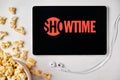 Showtime logo on the screen of the tablet laying on the white table and sprinkled popcorn on it. Apple earphones near