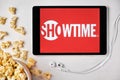 Showtime logo on the screen of the tablet laying on the white table and sprinkled popcorn on it. Apple earphones near