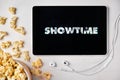 Showtime logo on the tablet screen laying on the white table with scattered popcorn and Apple earphones. Spending free