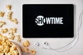 Showtime logo on the tablet screen laying on the white table with scattered popcorn and Apple earphones. Spending free