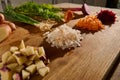 Shredded beet, carrot, onion and cubes of cut potato on a wooden board with halves of vegetables with green leaves and roots on