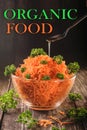 Shredded carrots with parsley in a transparent bowl on a dark wooden background, spoon with olive oil, vegetarian healthy food