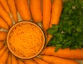 Shredded fresh carrots in a bowl with whole carrots around. Top view. Fresh carrot for backgrounds or textures