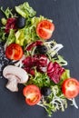 Shredded organic salad with cherry tomatoes over gray stone plate. Top view