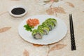 Shrimp and avocado rolls on a white plate with salmon decoration, soy sauce and black chopsticks in rustic table. Royalty Free Stock Photo