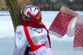 Shrovetide doll in colorful headscarf and sarafan near tree