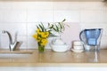 Tecoma stans flowers in a glass beaker on a white table in the interior. White bowls and cups, water filter on a