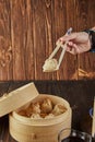 Shumai shaomai Chinese meat dumplings steamed in a bamboo steamer. Hand with chopsticks holding dim sum Royalty Free Stock Photo