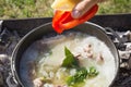 Shurpa soup in a large cast-iron cauldron outdoor. Cooking. Mens hand put ingredients for soup. Royalty Free Stock Photo