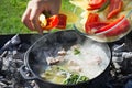 Shurpa soup in a large cast-iron cauldron outdoor. Cooking. Mens hand put ingredients for soup. Royalty Free Stock Photo