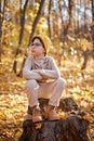 Cute kid boy in warm clothes sits on stump in autumn forest, enjoys a sunny day Royalty Free Stock Photo