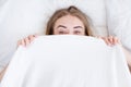 Shy cute lovely young woman, girl with lying in bed and hiding her face behind blanket.Rest,sleeping,people and comfort concept. B Royalty Free Stock Photo