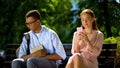 Shy geek sitting on bench with beautiful girl using smartphone, hesitation