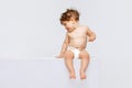 Portrait of little cute toddler boy, baby in diaper joyfully sitting and laughing isolated over white studio background Royalty Free Stock Photo