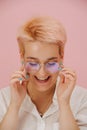 Shy happy young woman with short blond hair, round glasses and stars eye makeup