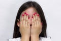 Shy little girl covers her face with hands showing pink polish nails Royalty Free Stock Photo