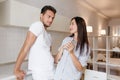 Shy long-haired female model in blue attire looking at husband with gently smile. Indoor portrait of european sporty man