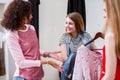 Shy smiling girl holding a pack of clothes listening to fashion stylist helping her picking outfit in a changing room Royalty Free Stock Photo